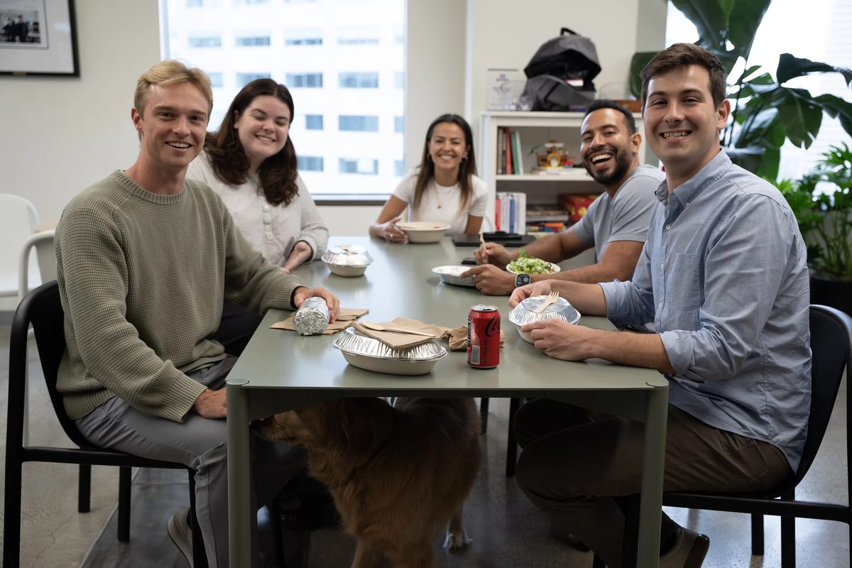 Five teammates around the lunch table, the office dog underneath